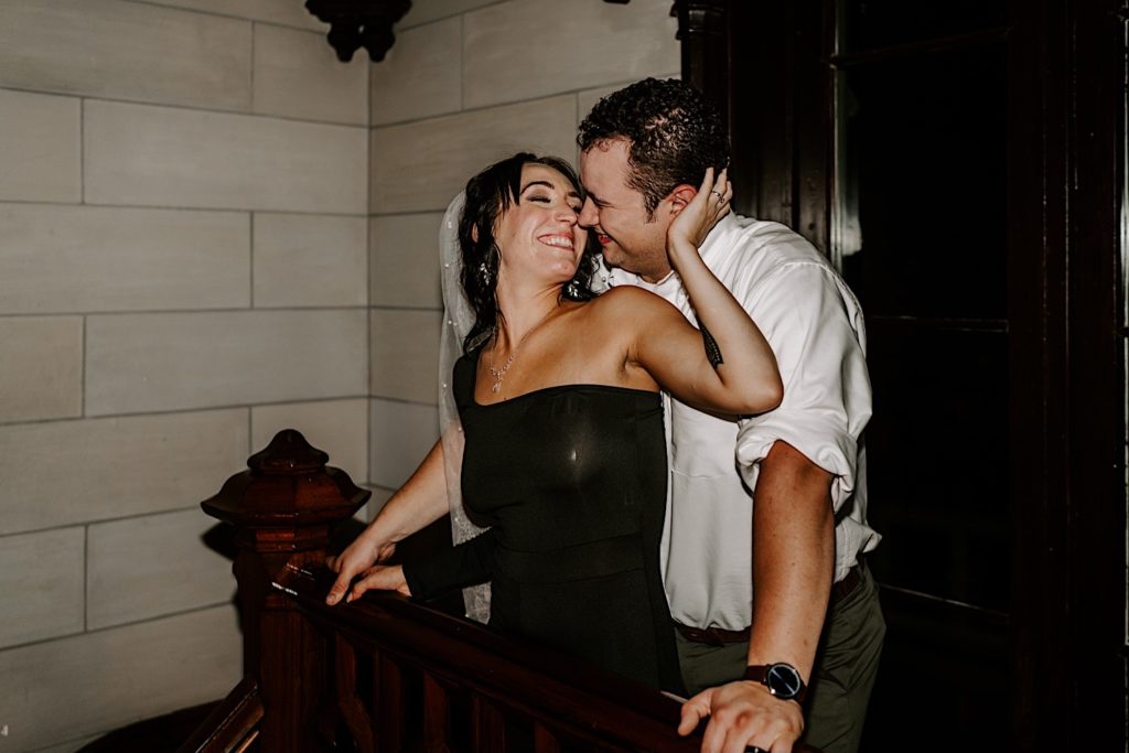 Couple smiles while about to kiss on their wedding day inside their wedding venue after the bride changed into a black dress.