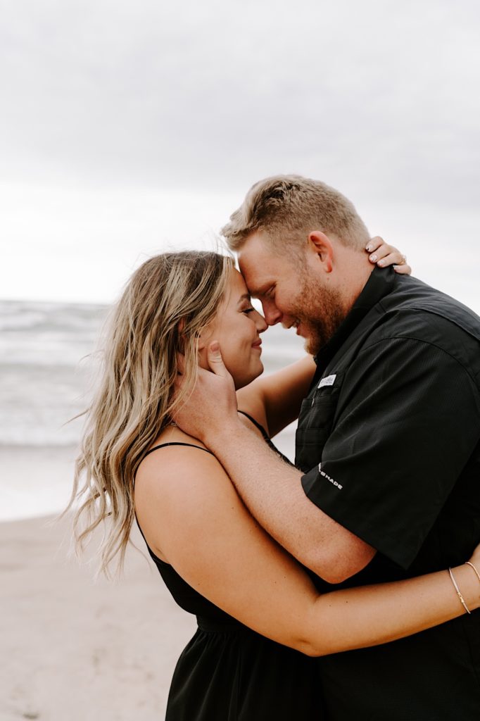 Bride and groom almost kiss during their engagement session on the beach overlooking Lake Michigan