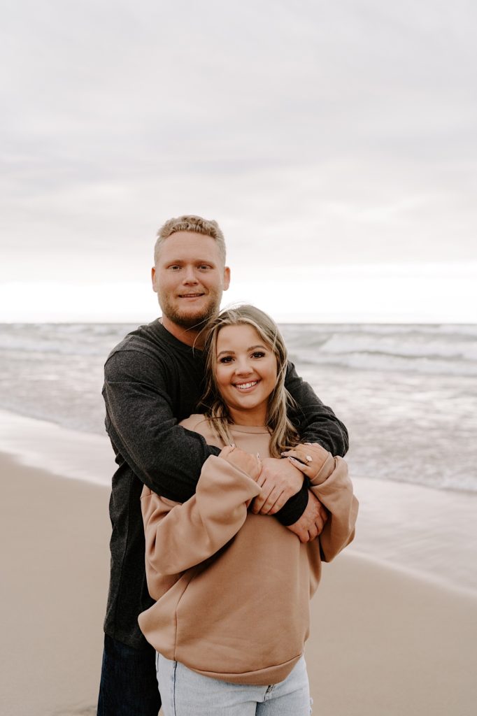 Fiancés hugging on the beach during their engagement session.