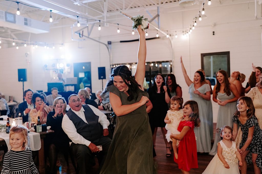 Girl in green dress catches bridal bouquet during a wedding reception.