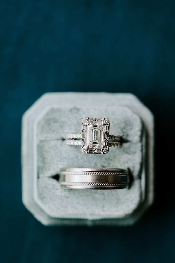 Emerald cut wedding ring with silver grooms wedding band in a sage colored box.