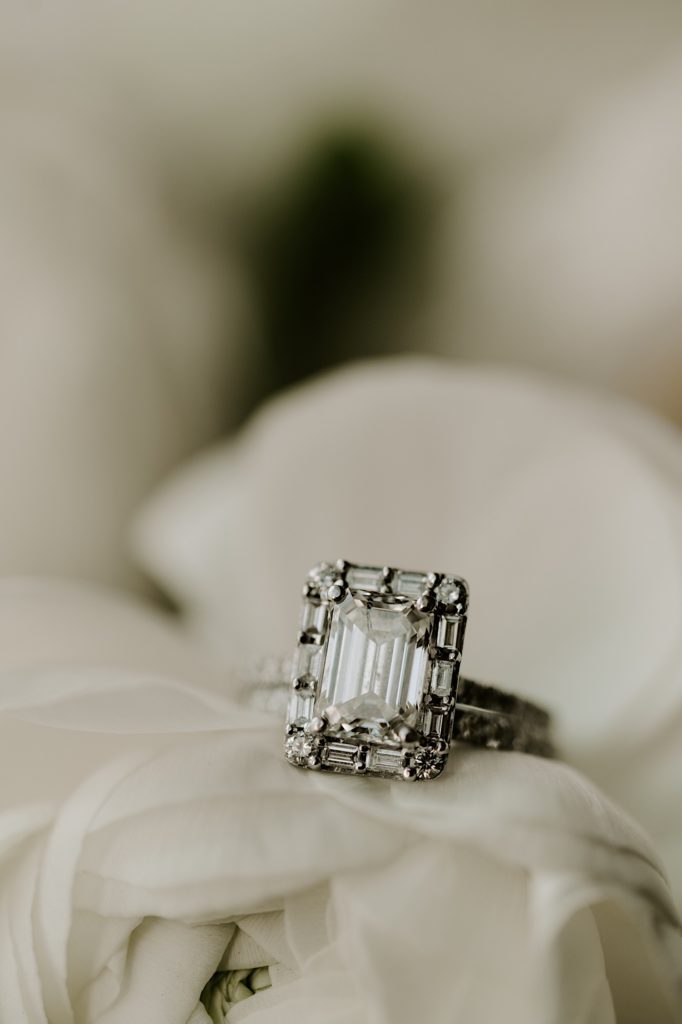 Emerald cut engagement ring sitting on ivory rose.