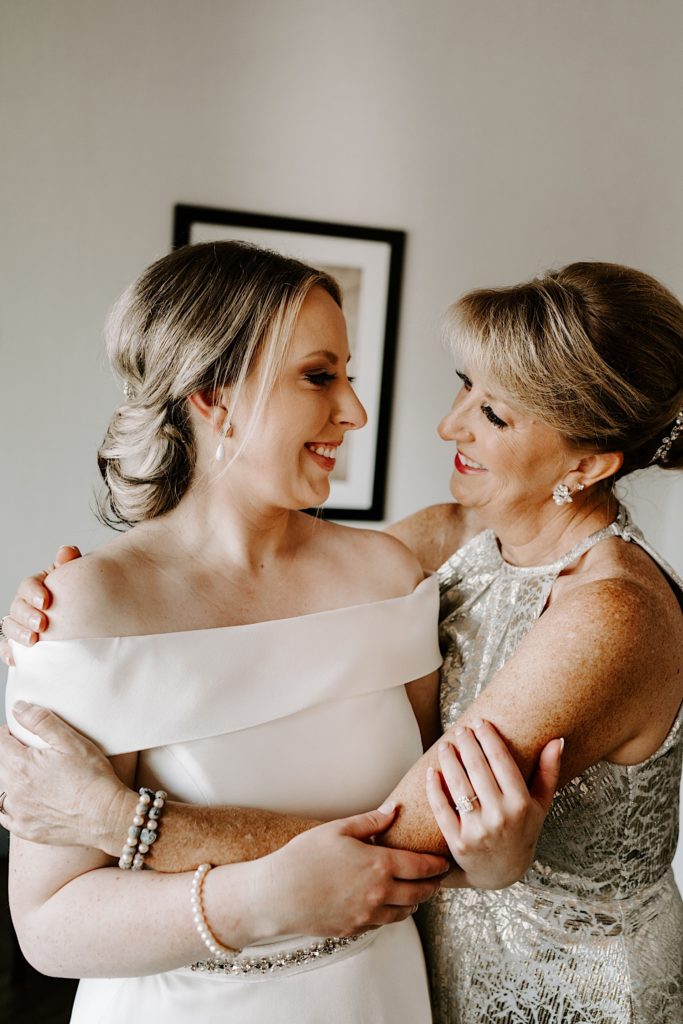 Bride hugs her mom in her wedding dress while smiling at each other before she leaves for her Indiana wedding.