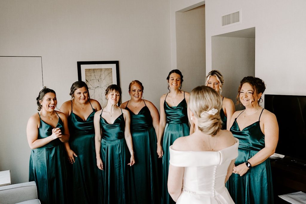 Bride has a first look with her bridesmaids who are dressed in emerald spaghetti strapped bridesmaids dresses.