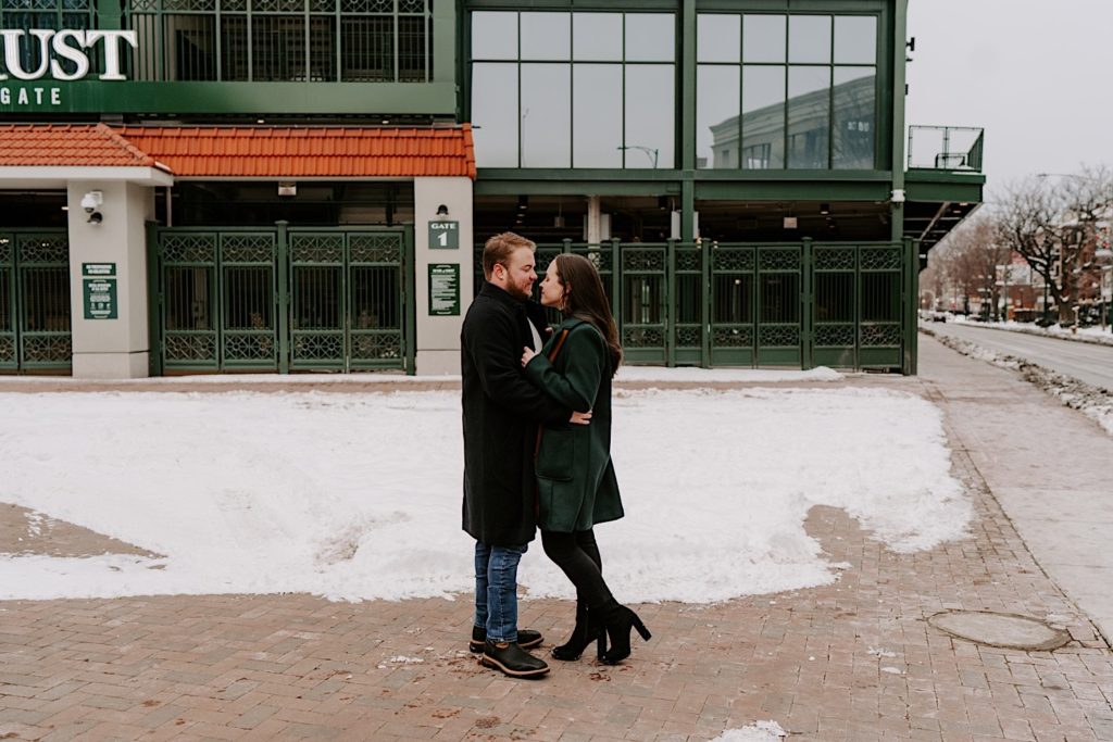 Couple stands outside of Wrigley Field standing facing each other during their engagement session.