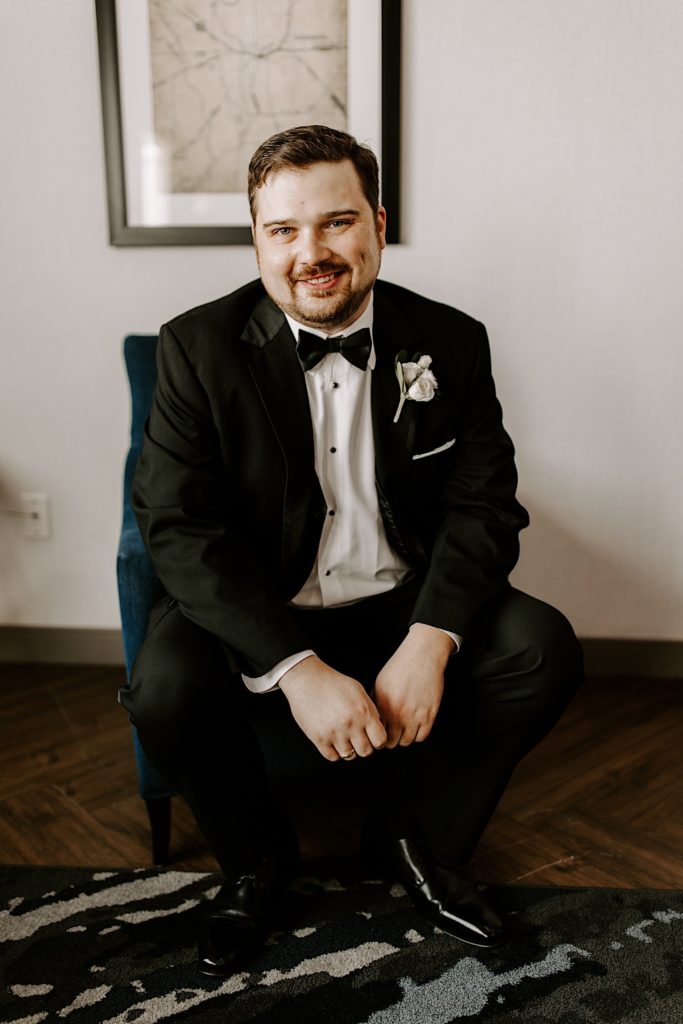 Groom sits smiling at the camera with his formal attire on.