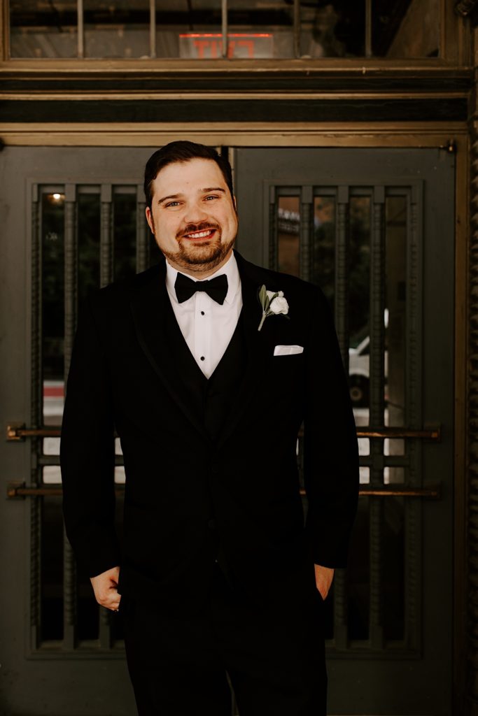 Groom smiles at the camera while standing outside the Indianapolis theater waiting for his bride to arrive for their first look.