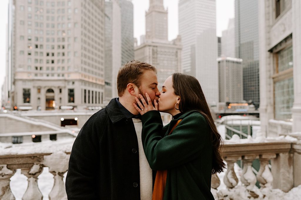 Engaged couple stands outside of Tribune Tower in Chicago kissing in the winter.