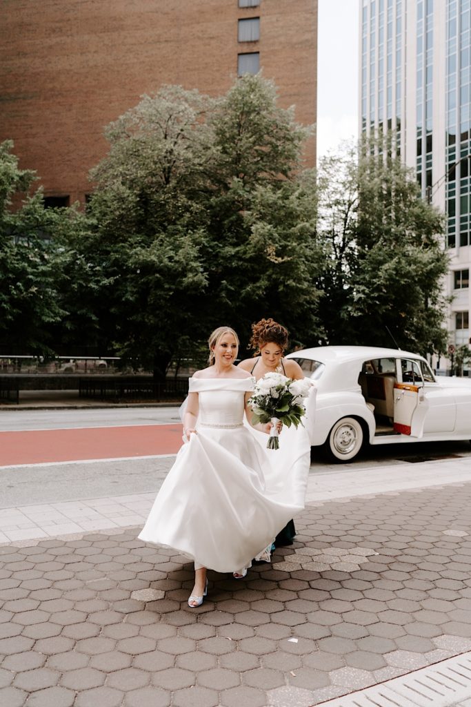Bride walks towards her groom with her bridesmaid holding her wedding dress train.
