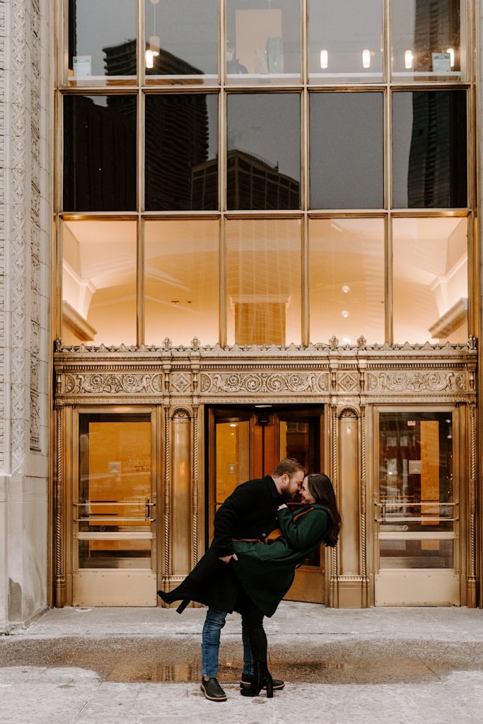 Couple dips outside the gold entrance of the Tribune Tower during their winter engagement session.
