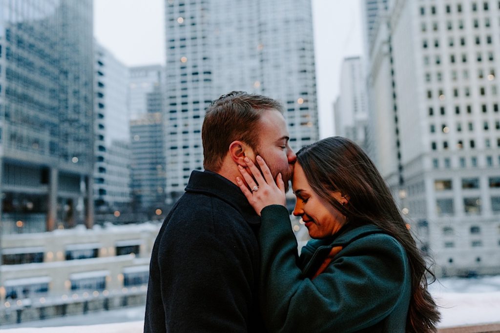 Fiance kisses his future bride on the forehead while standing by the Chicago Riverwalk.