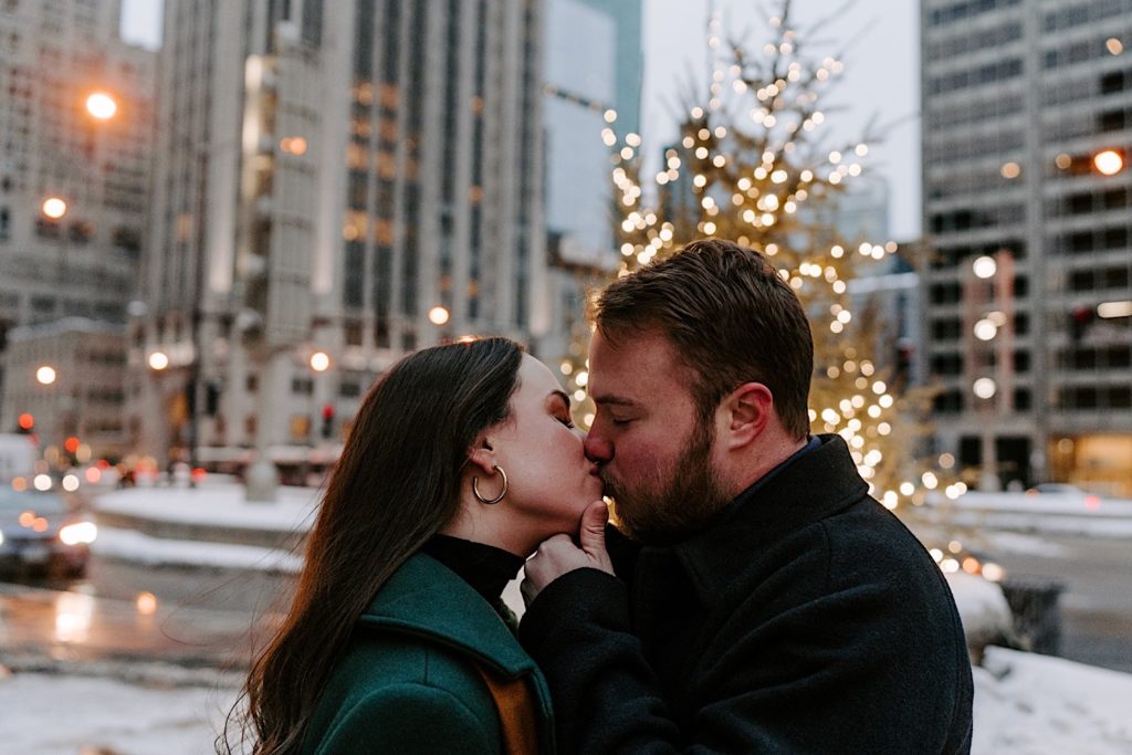 Couple kisses in front of holiday lights  during their winter engagement session in Chicago.