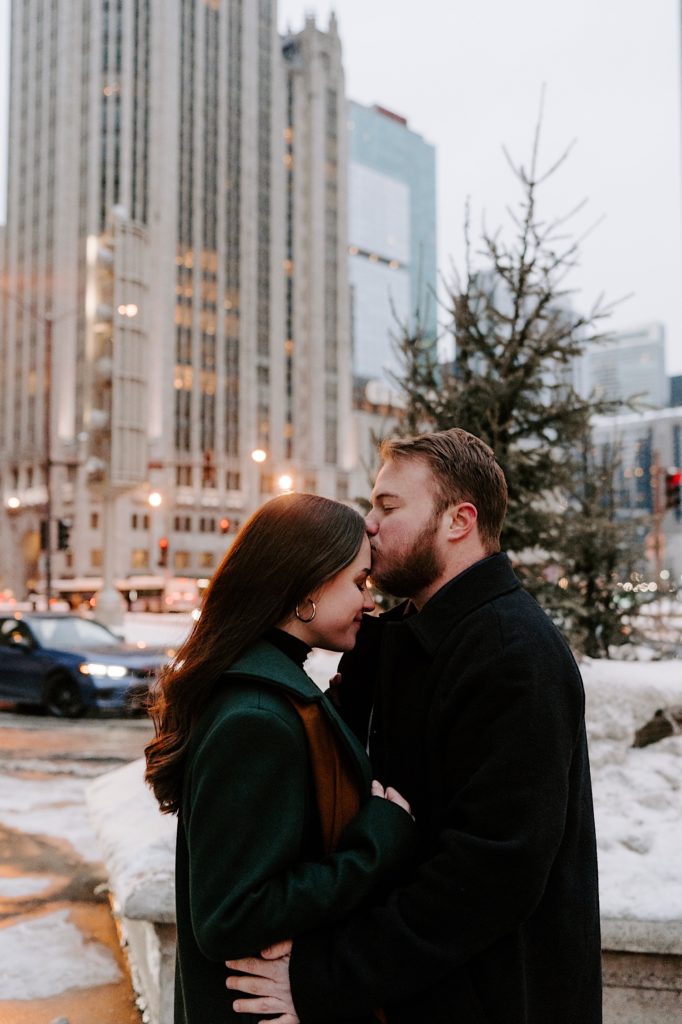 Couple stands in front of Christmas tree and fiance's kiss.