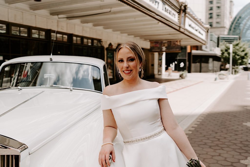 Bride leans up against a white 56 Rolls Royce outside the Indiana Repertory Theatre