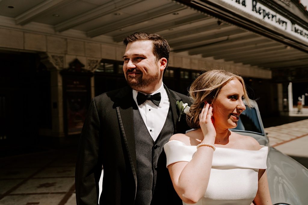 Bride and groom leans up against a white classic car for wedding portraits outside the Indiana Repertory Theatre