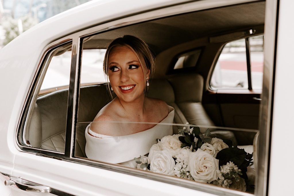 Bride sits in 56 Rolls Royce looking over her shoulder on her wedding day while holding her ivory bouquet.