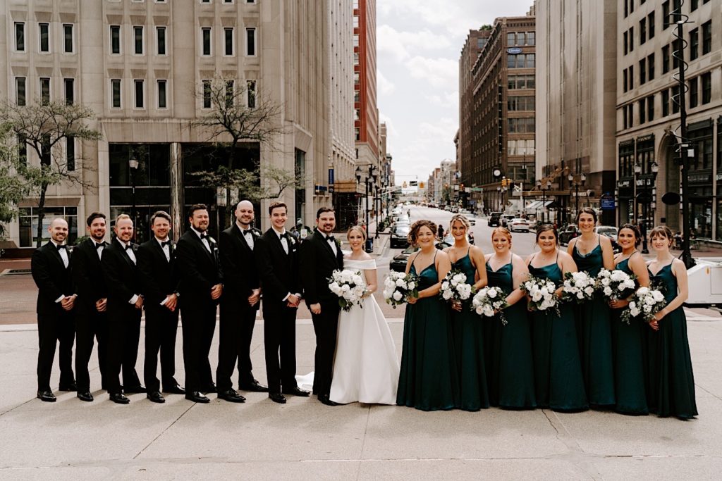 Bride and groom stand with their wedding party in the Monument circle  Indianapolis with the bridesmaids wearing emerald green bridesmaids dresses.