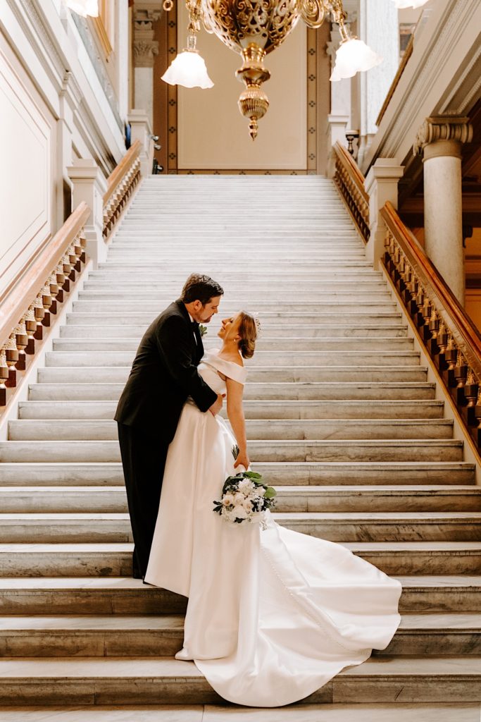 Bride and groom stand on a staircase at the Indianapolis state house embracing.