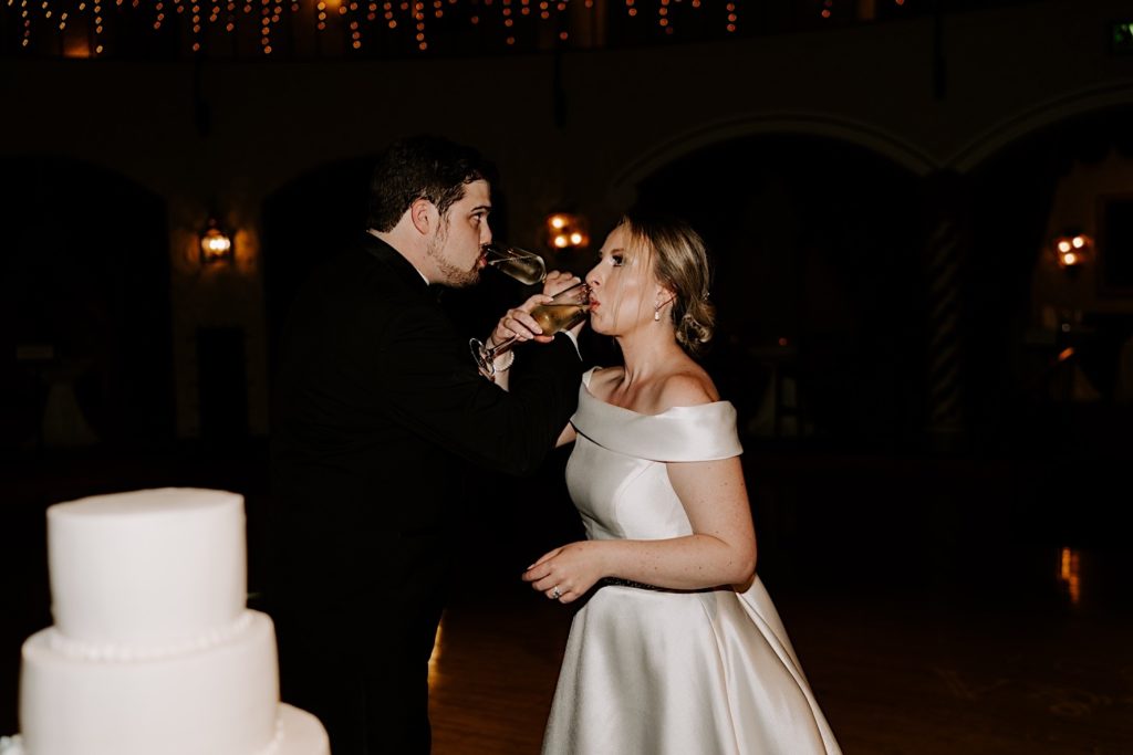 Bride and groom share a toast while standing in front of their wedding cake.