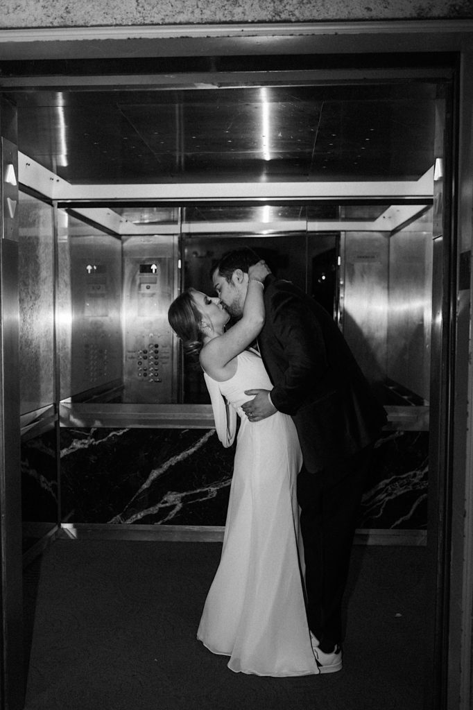A black and white image of a bride and groom kissing in an elevator on their wedding day.