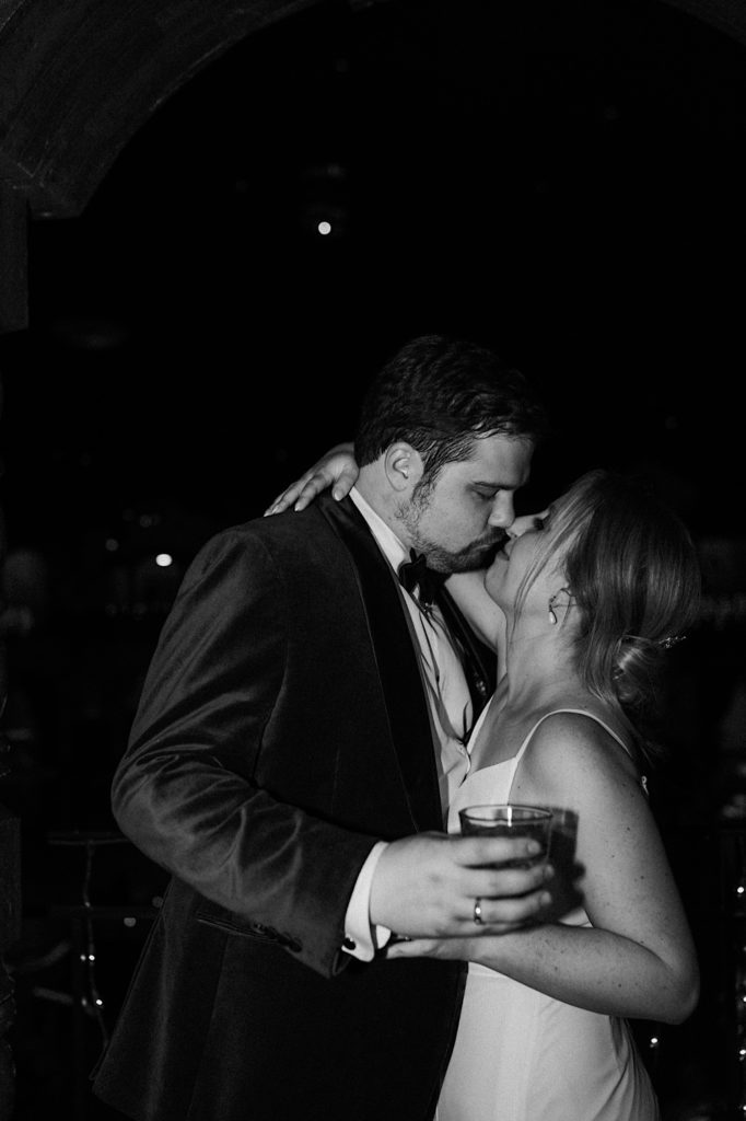 A black and white flash photo of the bride and groom kissing before heading back into their wedding reception.