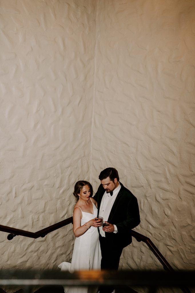Bride and groom share a toast in the stairwell while their share a moment outside their Indianapolis wedding reception