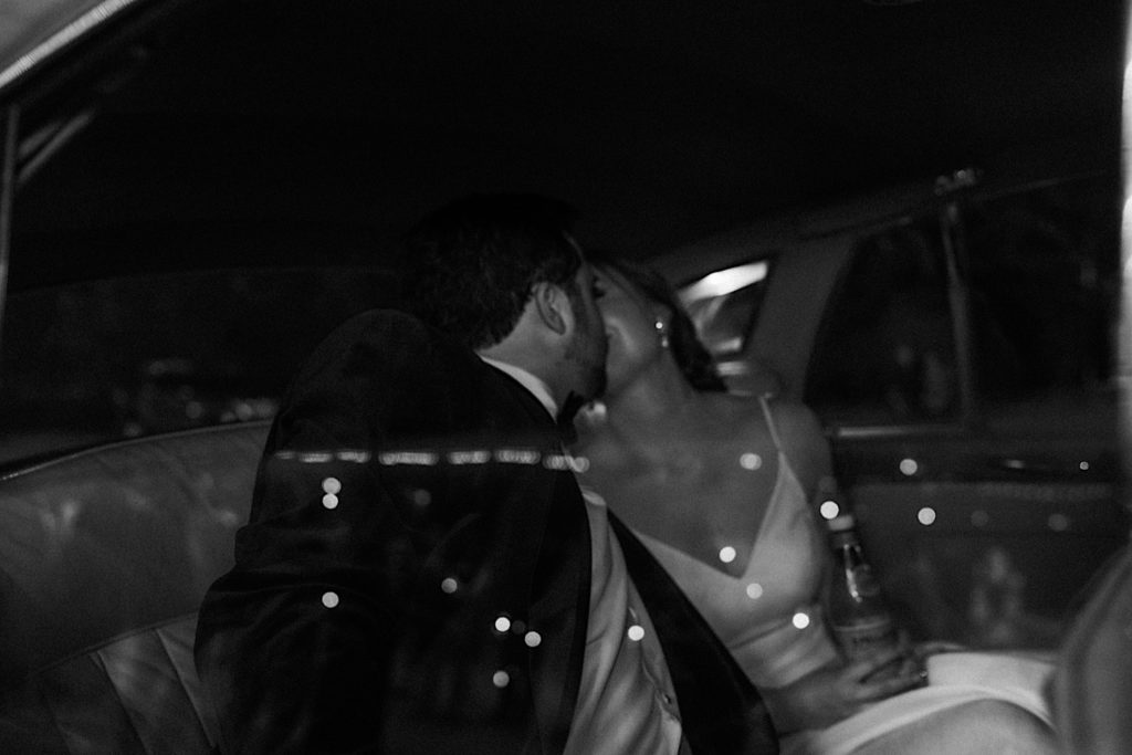 Black and white photo of a bride and groom kissing in their 56 Rolls Royce get away car after their Indiana Wedding