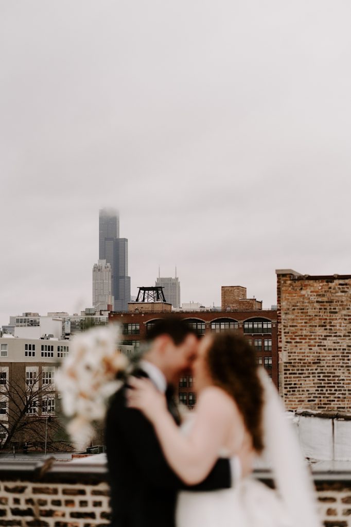 Bride and groom stand forehead to forehead with Chicagos' Willis tower in focus in the background.