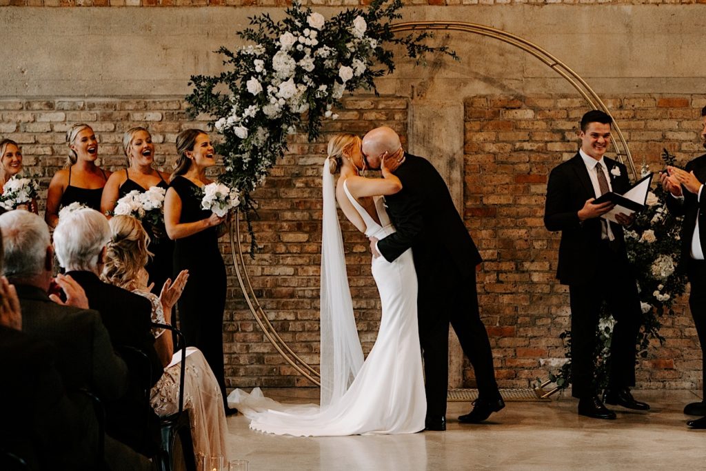 Bride and groom share a first kiss under their wedding arch at their urban Chicago venue