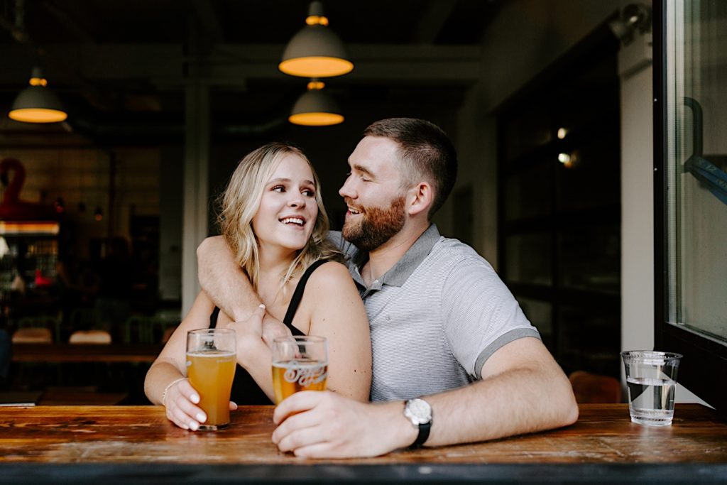 A couples smiles at one another during their Chicago engagement session at Begyle Brewery in Ravenswood