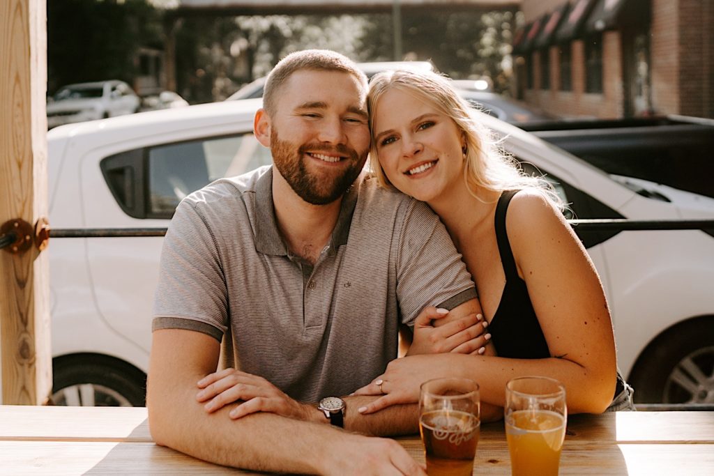 Engaged couple smiles at the camera during their engagement session at a Chicago brewery