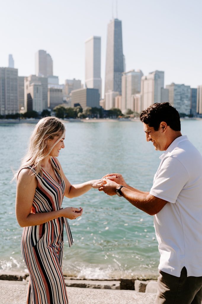 Fiancé puts a ring on his future bride standing in front of the Chicago skyline.