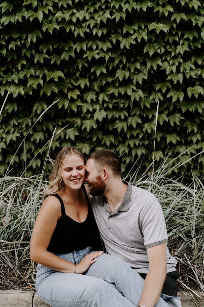 Couple sits in front of a wall covered in ivy while smiling in Ravenswood Chicago