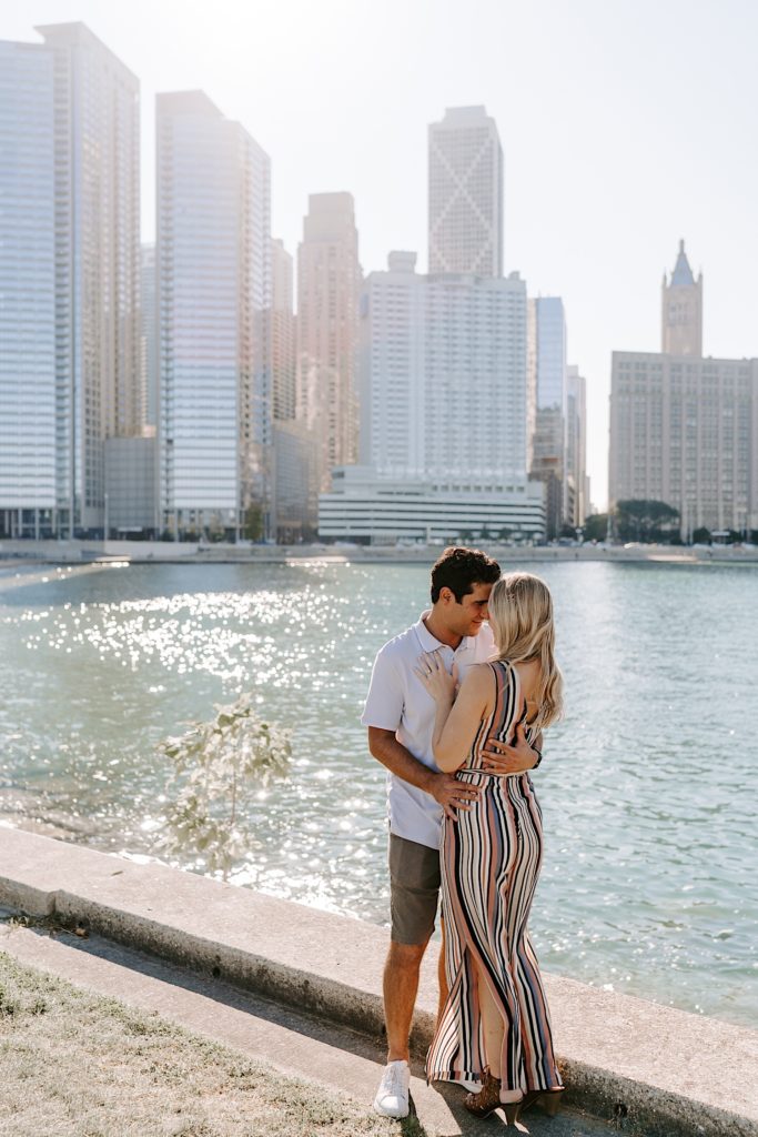 A wide photo of fiancés snuggle in tight and hug on the lake front in Chicago during their engagement session at Milton Lee Olive Park with the skyline in the background
