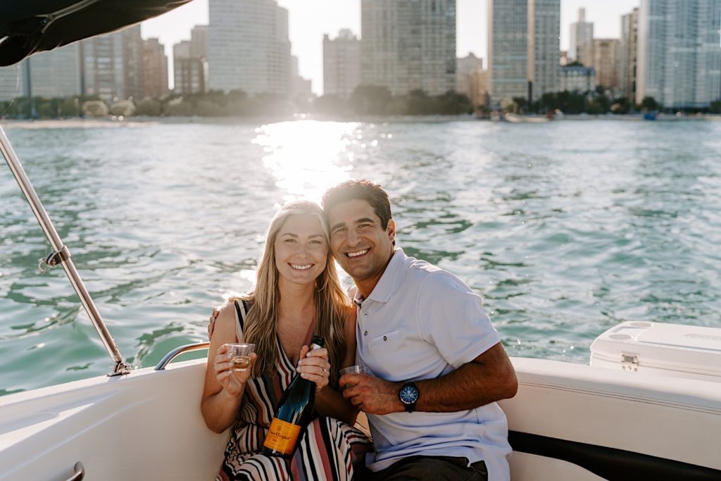 Fiancés sit on a small speedboat with champagne on lake Michigan during their engagement session in Chicago