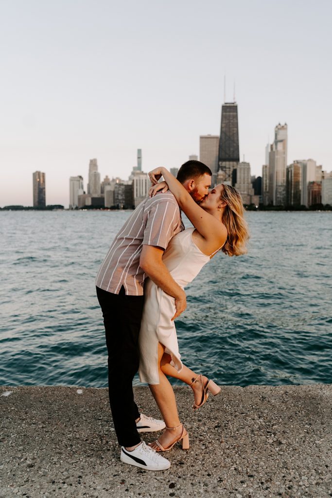 An engaged couple kisses and dips while standing on the ribbon at North Avenue Beach.
