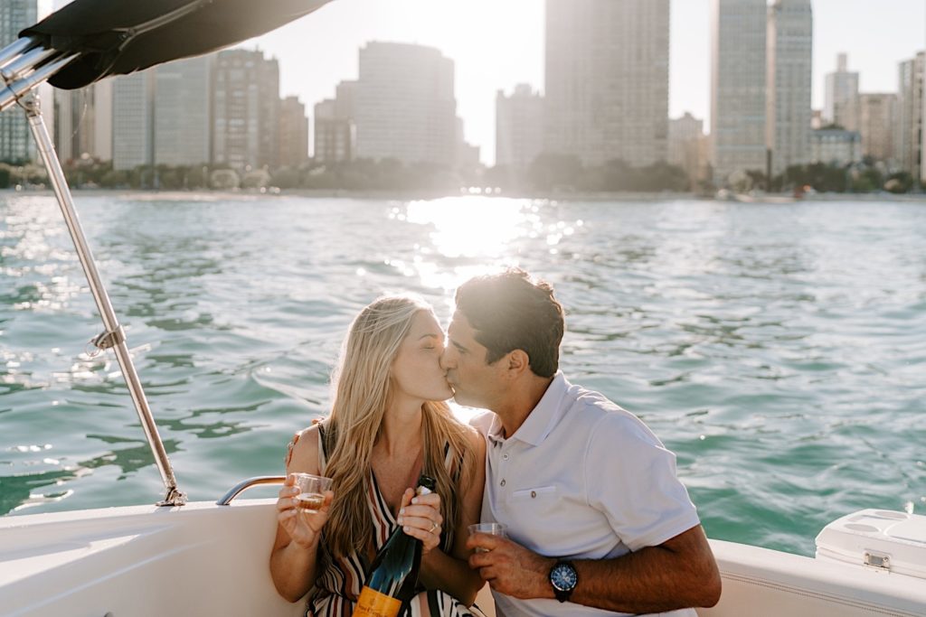 Fiancés sit kissing on a small speedboat with champagne on lake Michigan during their engagement session in Chicago