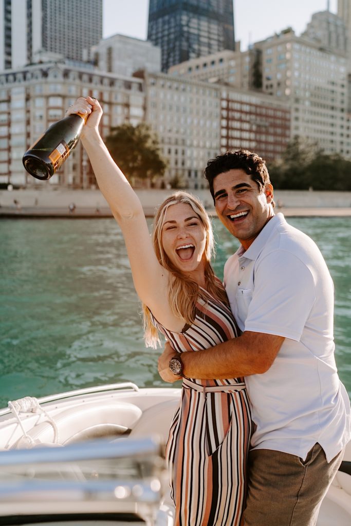 Fiancés shout at the camera while holding a bottle of champagne celebrating their Chicago proposal on a boat on lake Michigan