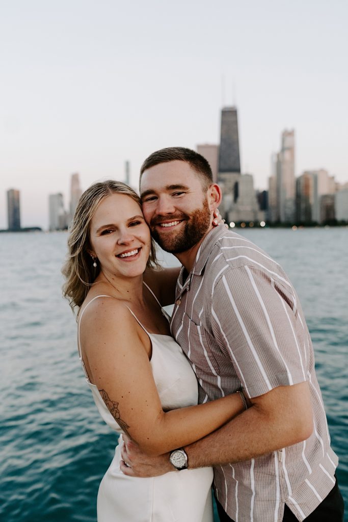 An engaged couple smiles at the camera during their engagement session in Chicago overlooking Lake Michigan