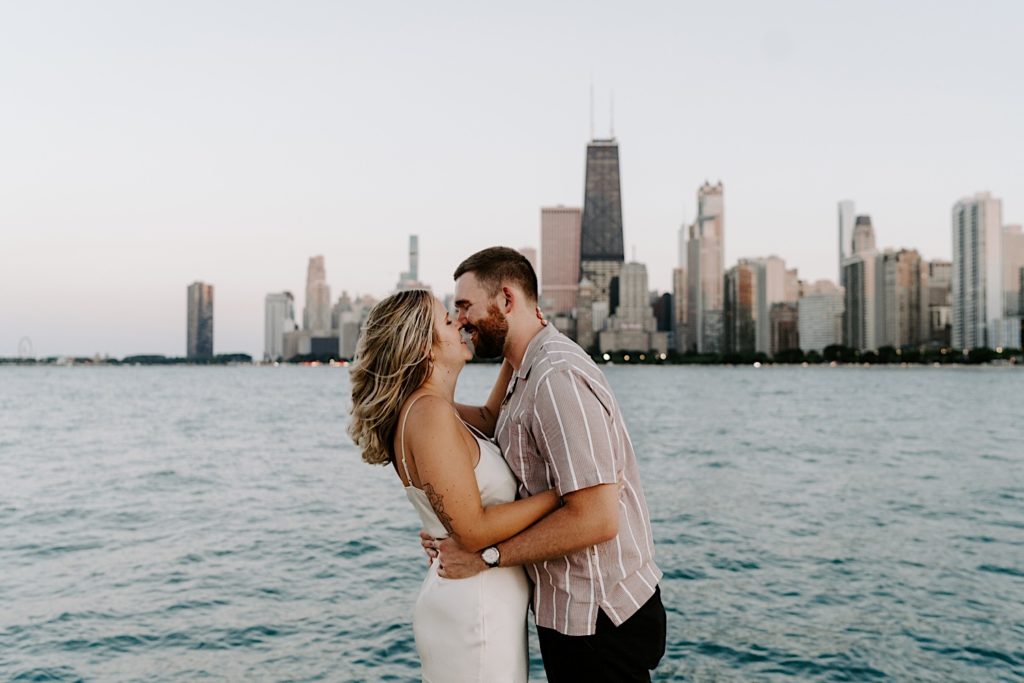 An engaged couple holds one another while almost kissing and you can see the Chicago skyline in the background overlooking Lake Michigan.