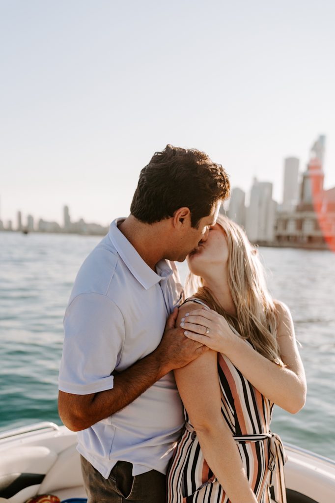 Fiancés kiss and hold each other tight on a boat admiring the Chicago skyline during their engagement session