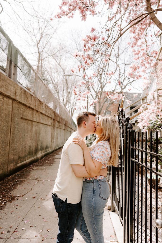 A fiancé holds his fiancée and kisses her after proposing in a Chicago neighborhood in the spring.