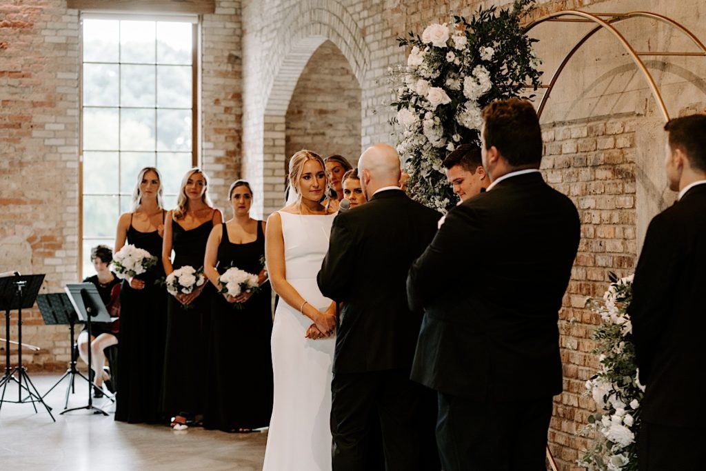 A couple stands facing each other during their wedding ceremony in front of a brick wall at their urban wedding venue in the Chicago suburbs