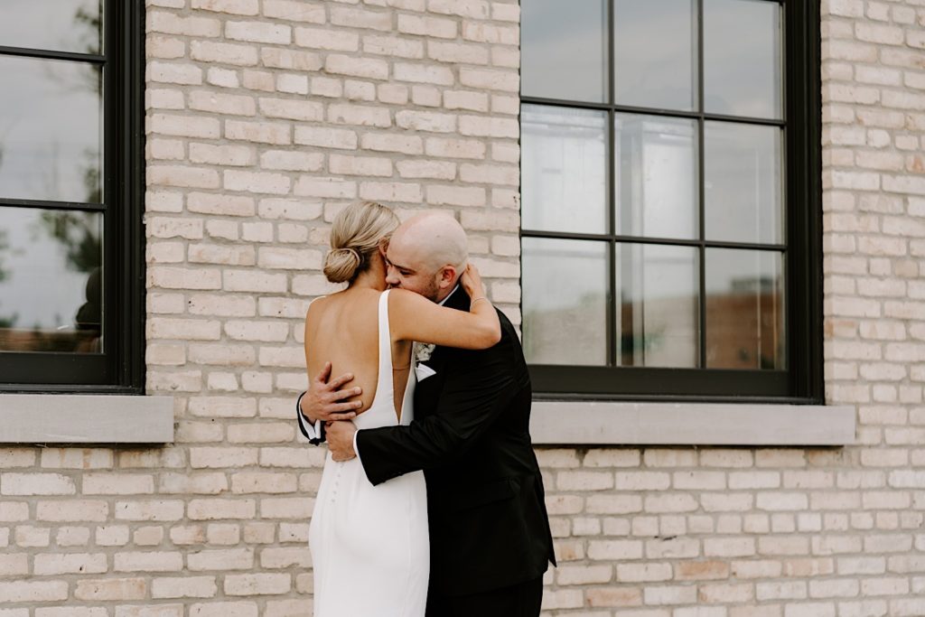 Newly-weds embrace in front of a brick wall outside of their wedding venue in Carpentersville Illinois