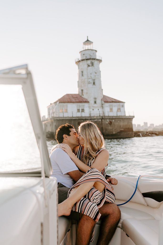 A newly engaged couple kisses while the fiancée sits on her fiancé's lap on a boat looking over Lake Michigan and the Chicago Skyline.