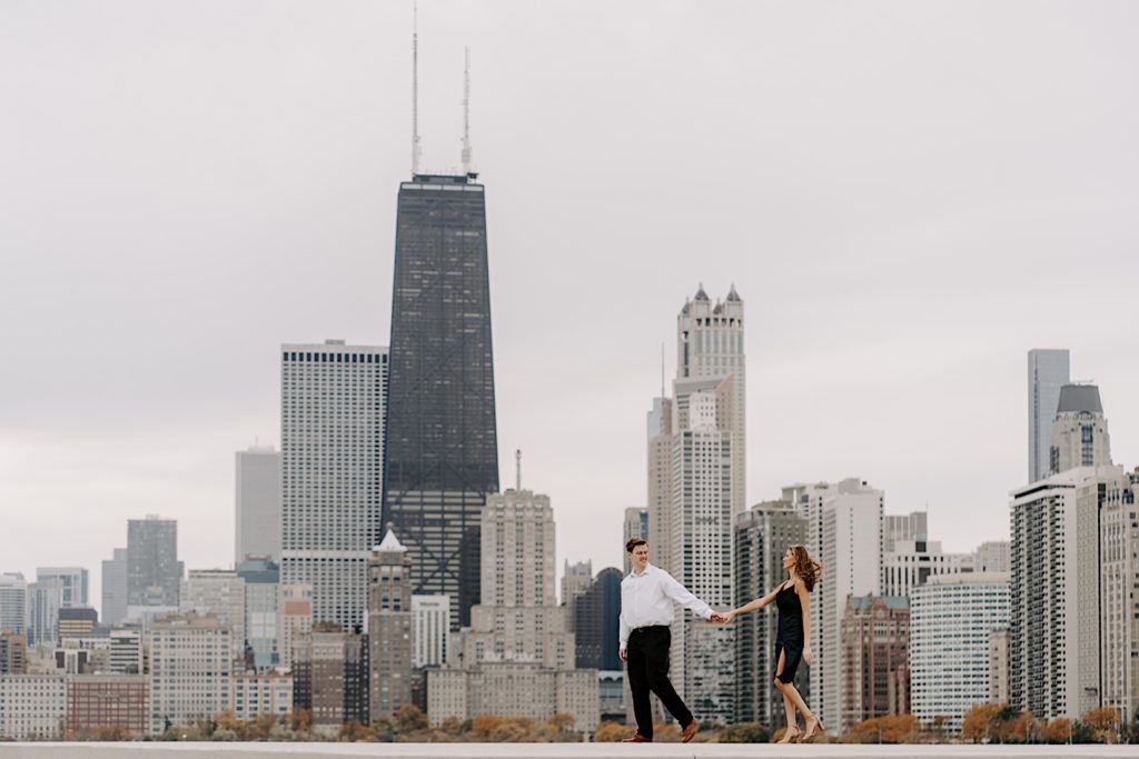 A future bride and groom walk past the Chicago skyline on the ribbon at North Avenue Beach.