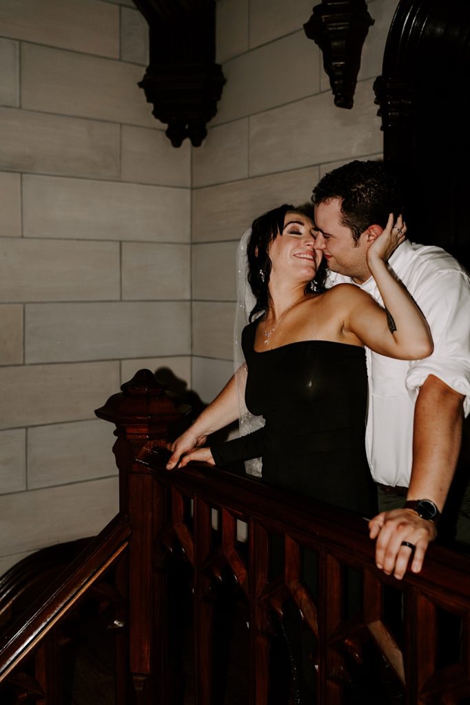 An engaged couple has fun inside a Chicago building during their engagement session.  They stand overlooking a banister almost kissing.