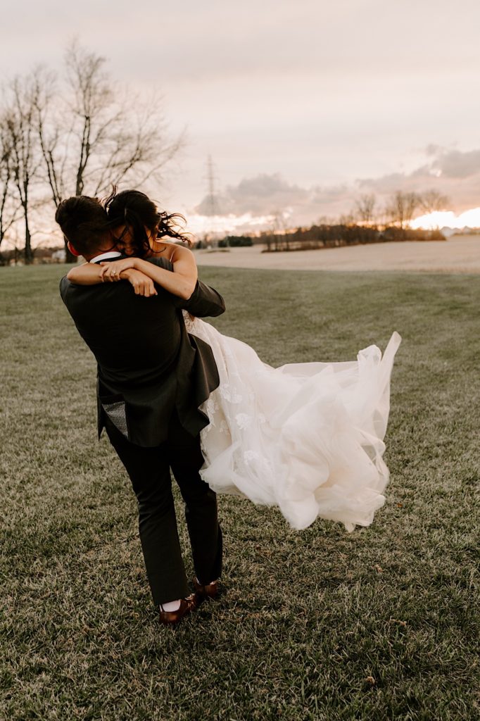 A groom hugs his bride and spins her during sunset portraits on their wedding day.