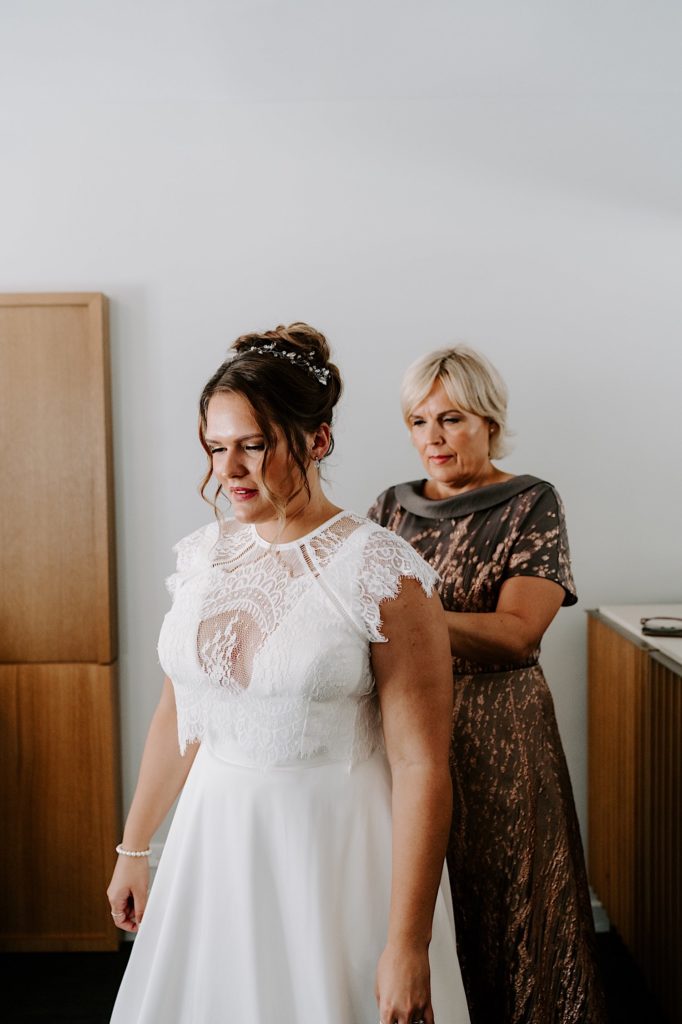 A bride has her mother help her put on the finishing touches to her wedding dress.