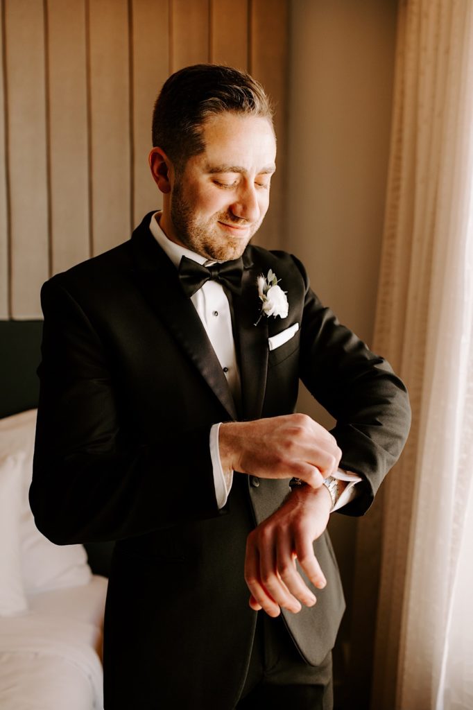 A groom puts on his watch in his wedding day tuxedo before his wedding ceremony.